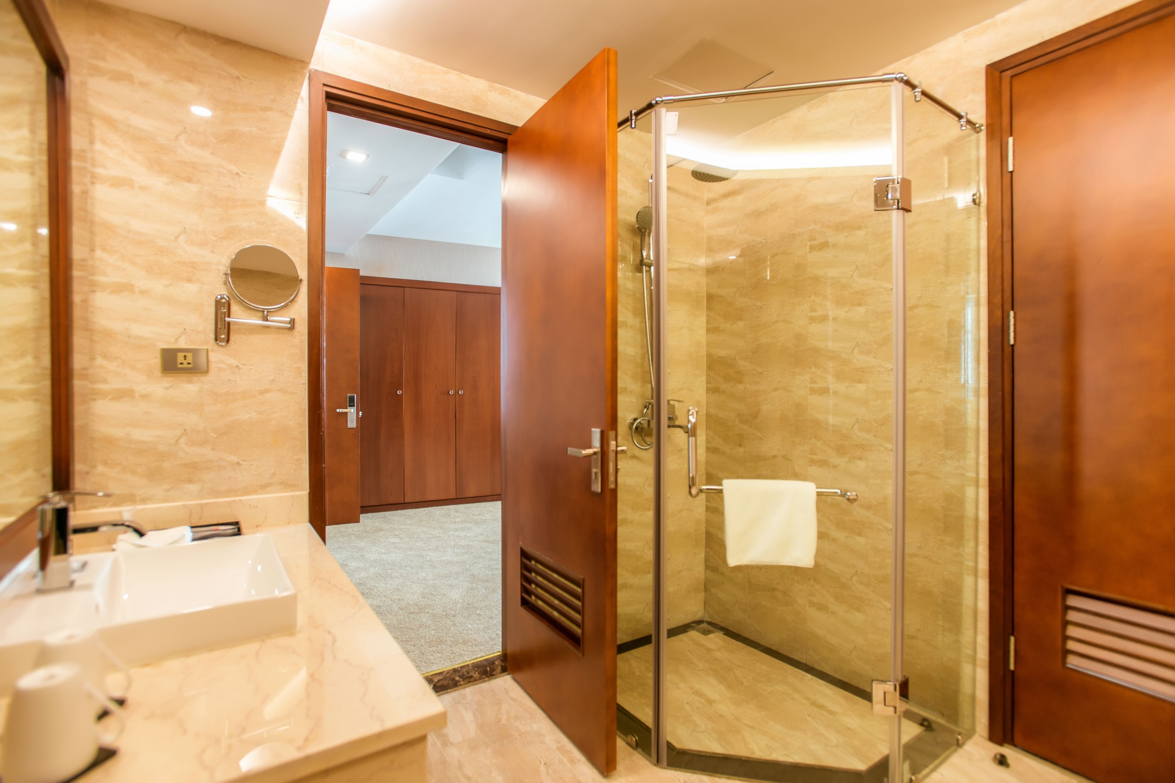 A modern bathroom with a glass-enclosed shower, a marble sink, and wooden doors.