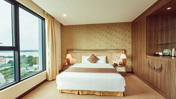 A hotel room with a large bed, two bedside tables with lamps, a wardrobe, and a view of the city through a large window.