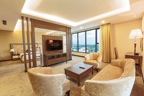 Habitación de hotel con televisor grande, asientos cómodos, vista a la ciudad y diseño moderno.