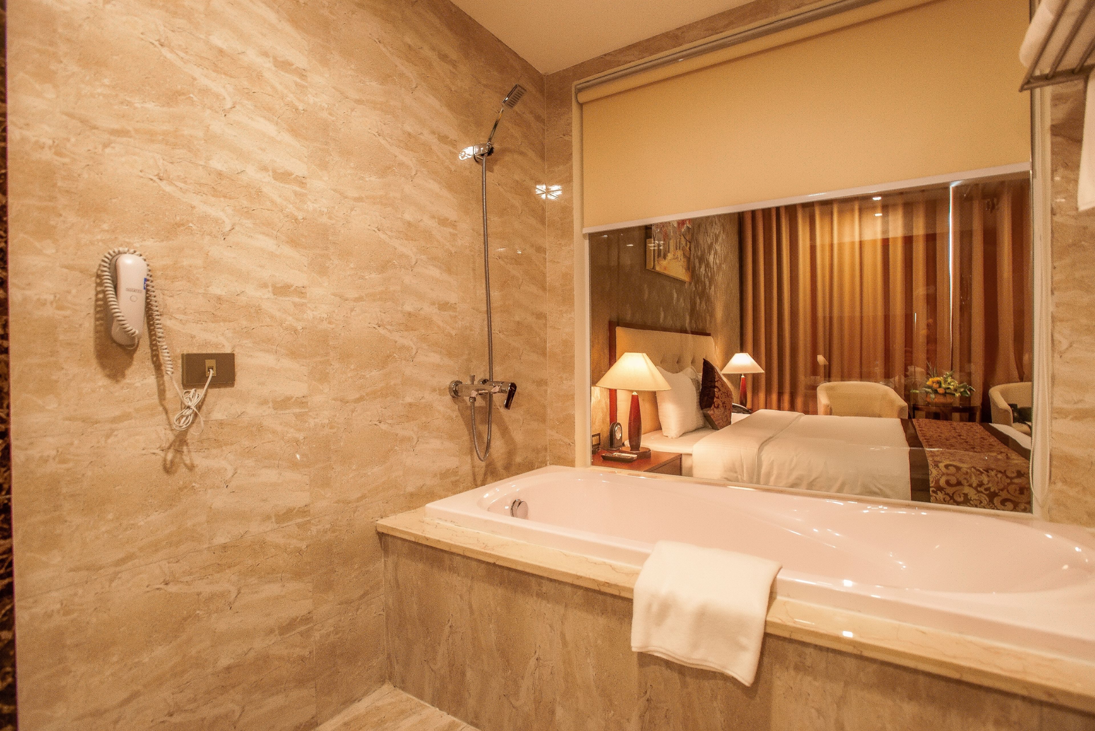 A modern bathroom with a large bathtub, a showerhead, and a hand dryer on the wall.