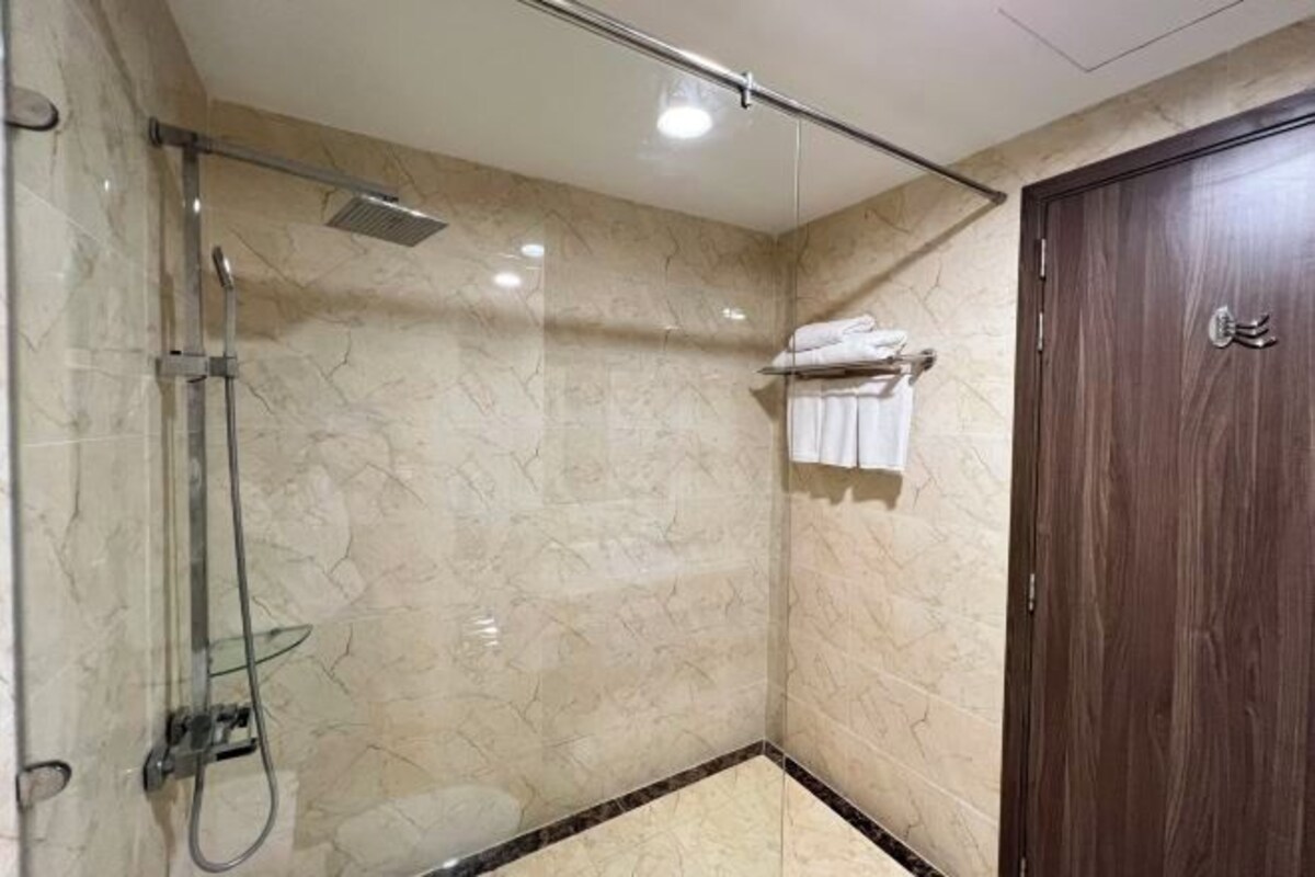 Un baño con ducha de vidrio, paredes de mármol y puerta de madera.