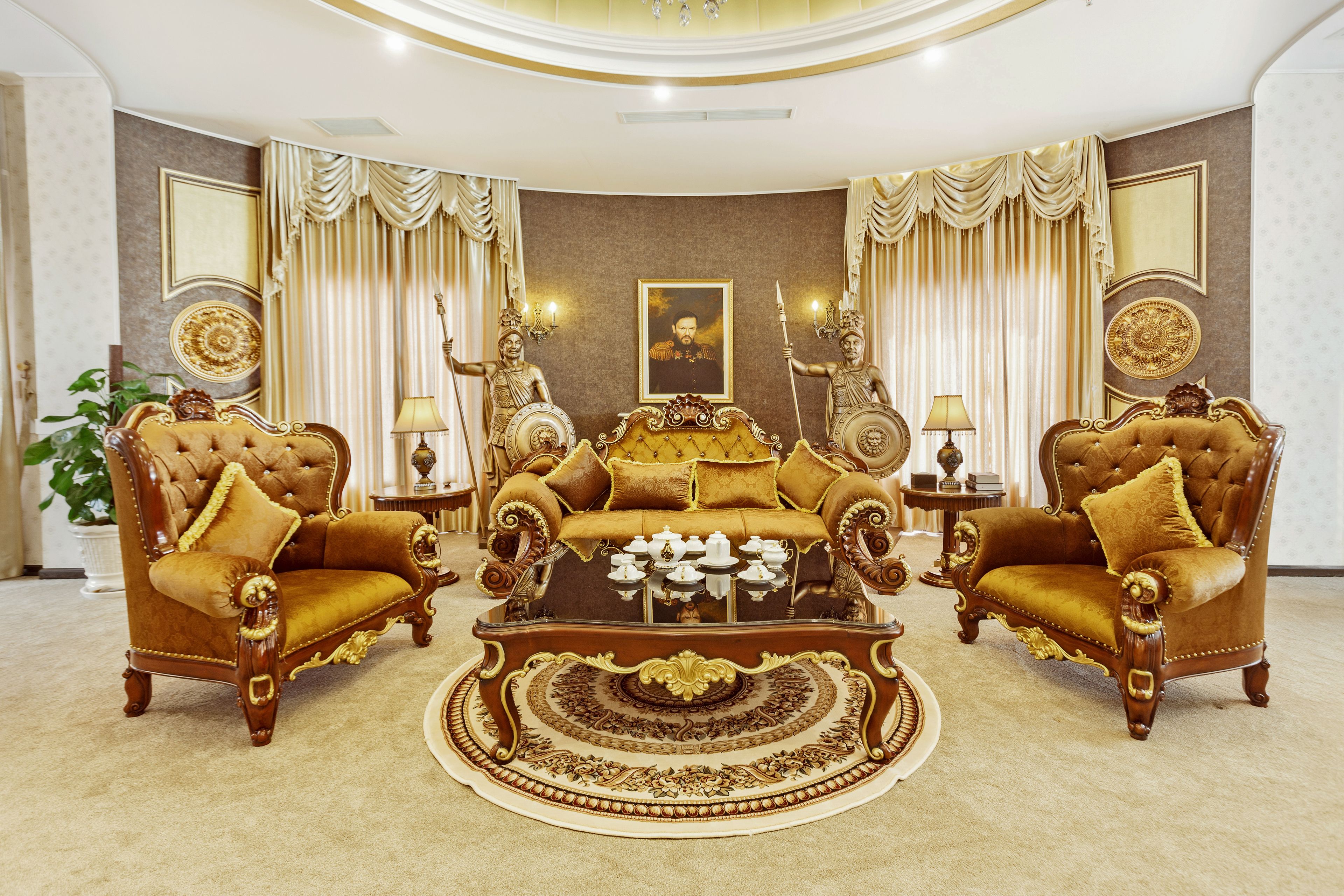 A luxurious living room with a large, ornate sofa set, two matching armchairs, and a coffee table with decorative items.