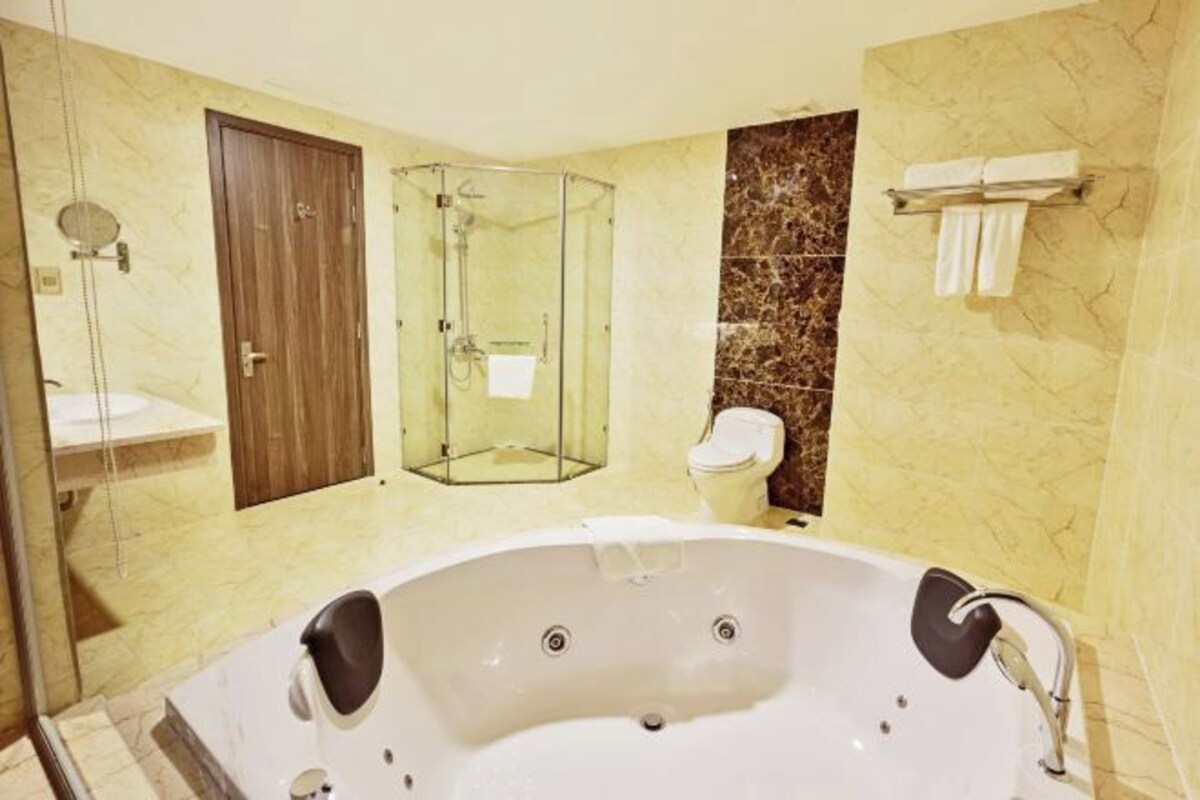 Un baño con una bañera grande, ducha con cerramiento de vidrio, inodoro y puerta de madera.