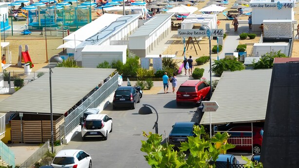 A beachside hotel with rows of beach umbrellas, a pier, and a parking area with cars. - Hotel Sanremo (Rimini)