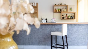 A bar area with a coffee machine, shelves with bottles, a white chair, and a vase with flowers. - Hotel Sanremo (Rimini)