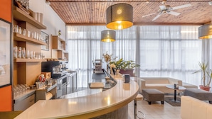 A modern kitchen with a curved counter, a coffee machine, and a dining area with a sofa and ottoman. - Hotel Sanremo (Rimini)