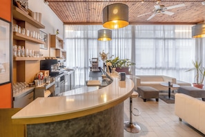 Una cocina moderna con una encimera curva, una cafetera y un comedor con sofá y reposapiés.