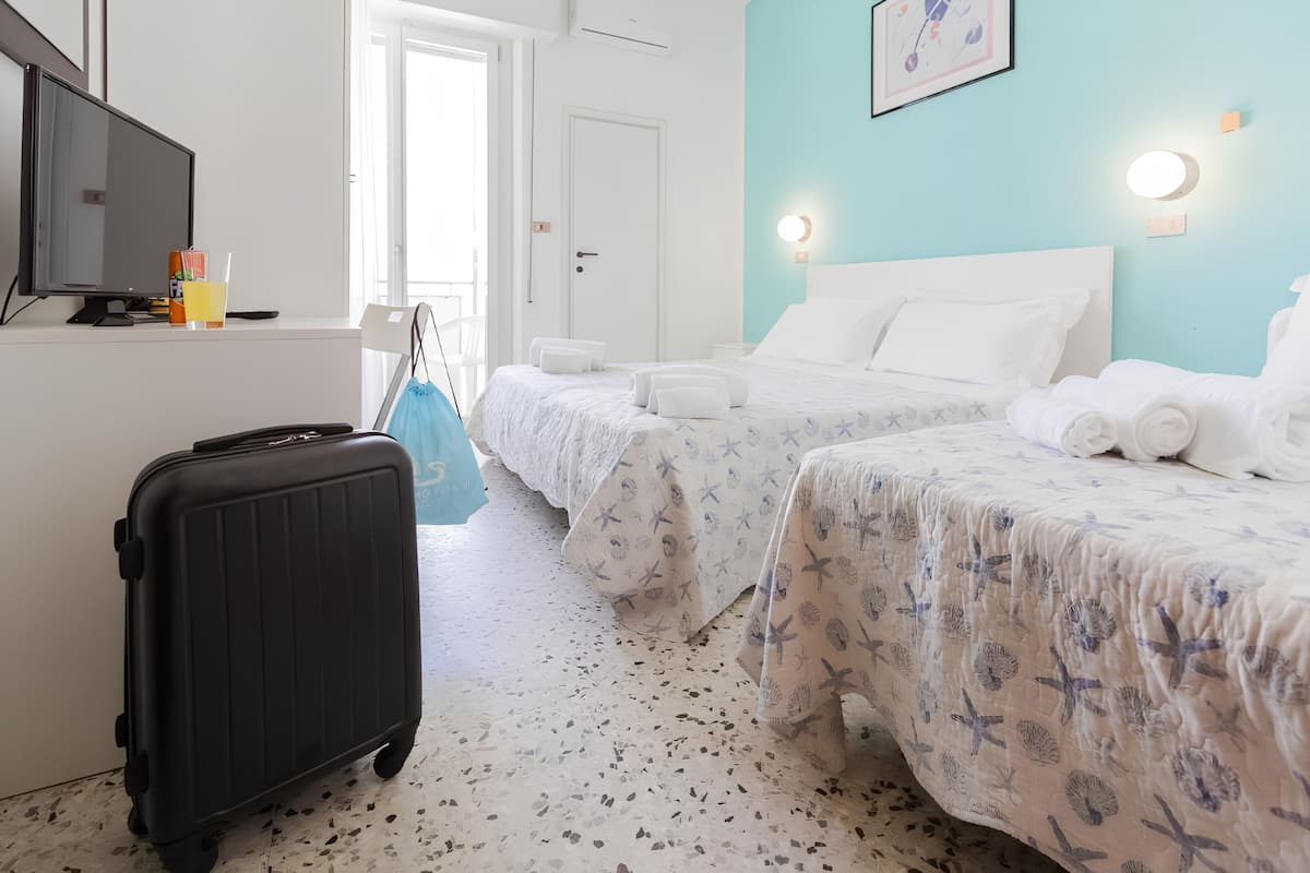 Habitación de hotel con cama, escritorio, computadora, maleta y puerta.