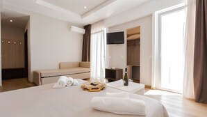 A hotel room with a bed, a sofa, a TV, and a desk with a bottle and glasses. - Hotel Sanremo (Rimini)