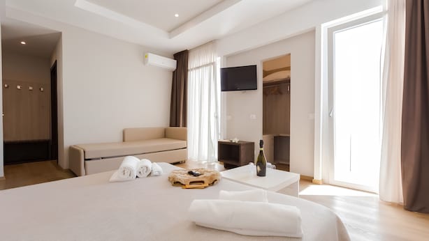 A hotel room with a bed, a sofa, a TV, and a desk with a bottle and glasses. - Hotel Sanremo (Rimini)