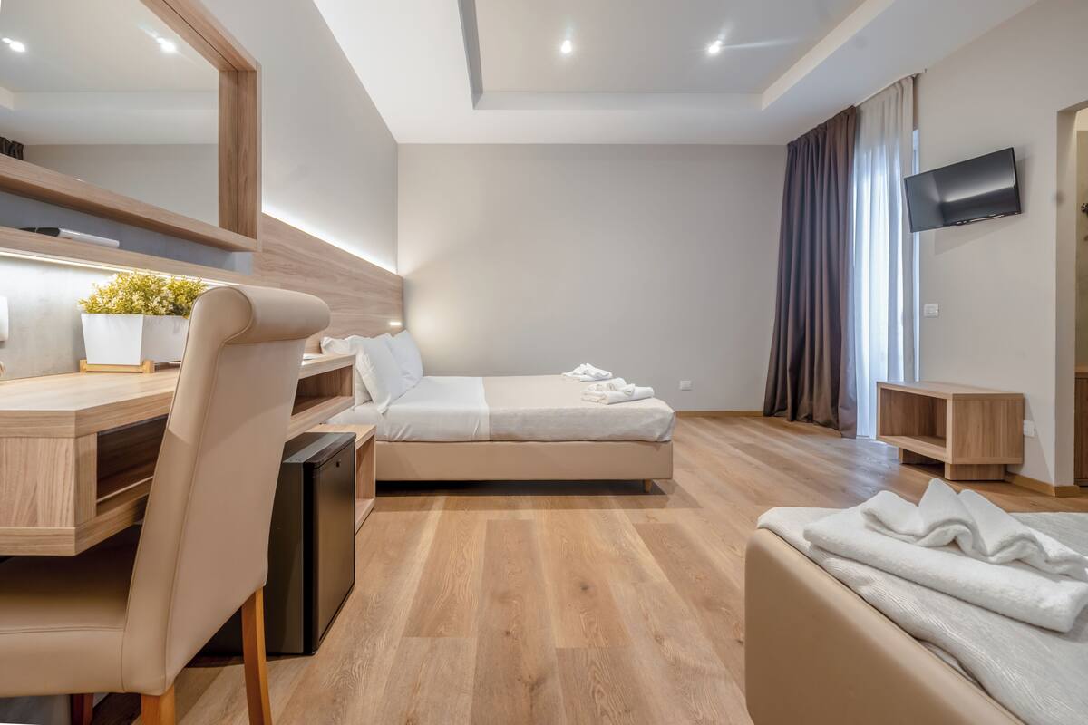 Una habitación de hotel moderna con cama, escritorio, silla, televisor y un pequeño mueble de madera.