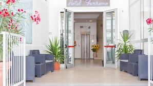 A hotel entrance with a sign reading 'Hotel L'Impero,' glass doors, wicker furniture, potted plants, and a push bar. - Hotel Sanremo (Rimini)