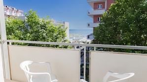 A balcony with two white plastic chairs and a table, overlooking a cityscape with buildings and trees. - Hotel Sanremo (Rimini)