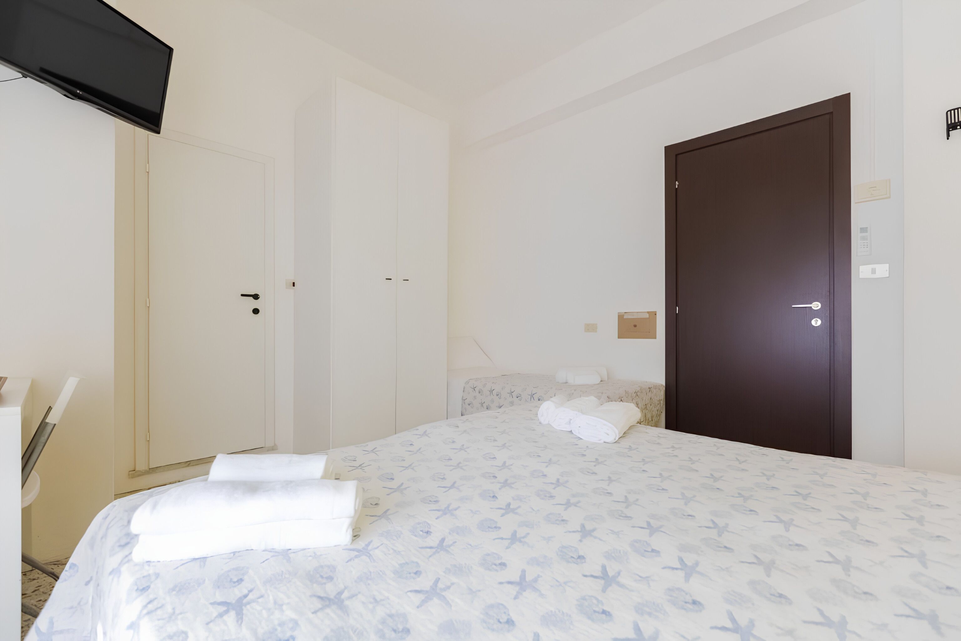 A hotel room with a bed, a wardrobe, a door, and a flat-screen TV.
