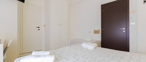 A hotel room with a bed, a wardrobe, a door, and a flat-screen TV.