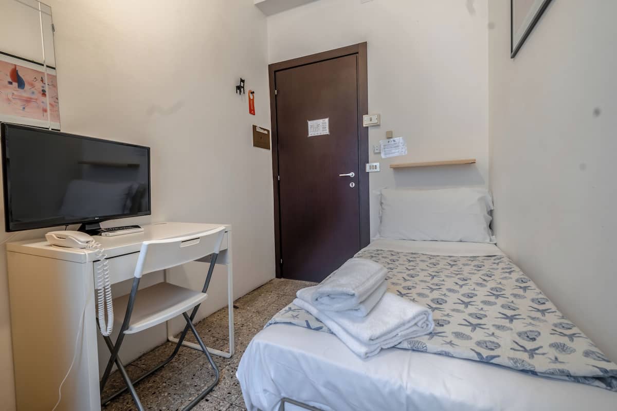 Una habitación de hotel pequeña con cama, escritorio con televisor, una silla y una puerta.