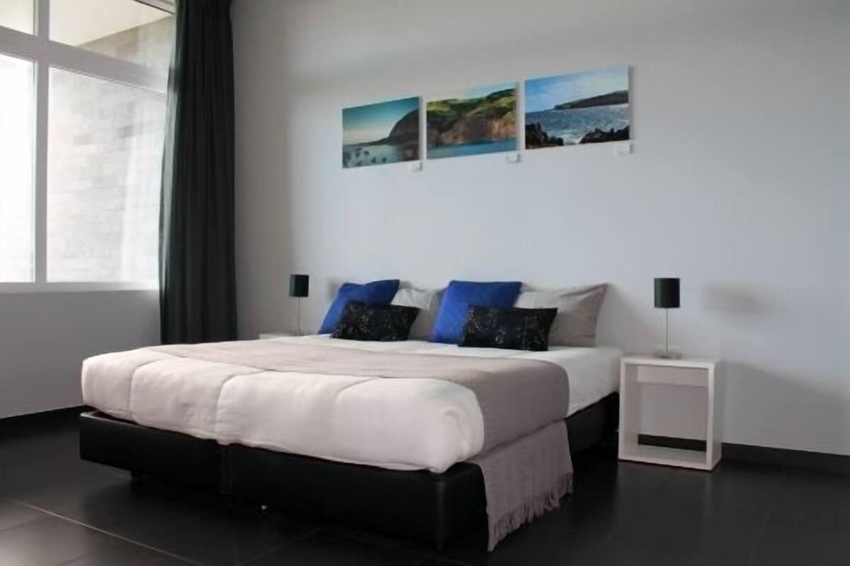 Un dormitorio moderno con una cama grande, una mesita de noche y una ventana con cortinas.