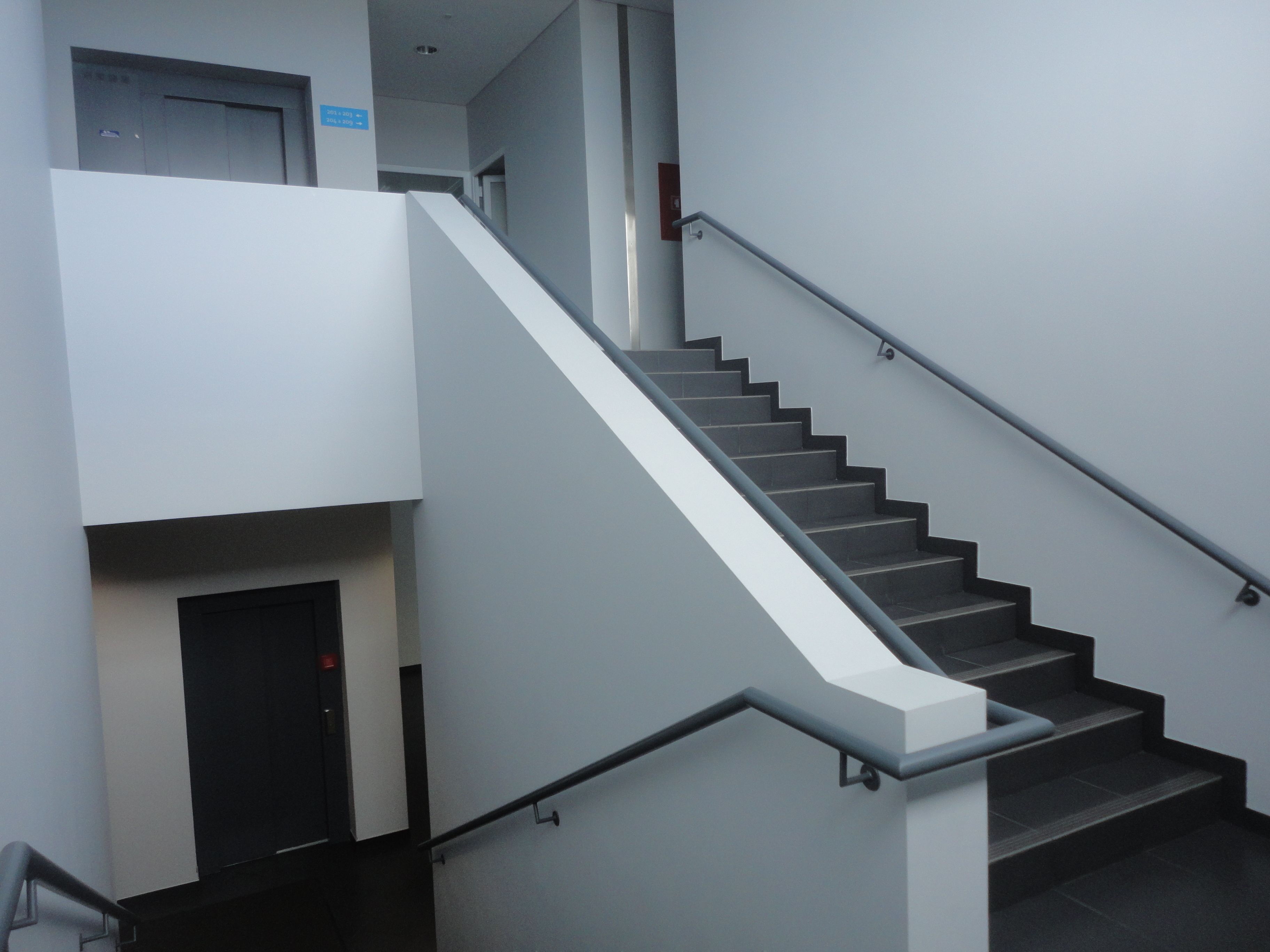 Een moderne trap met een leuning, die leidt naar een lift.