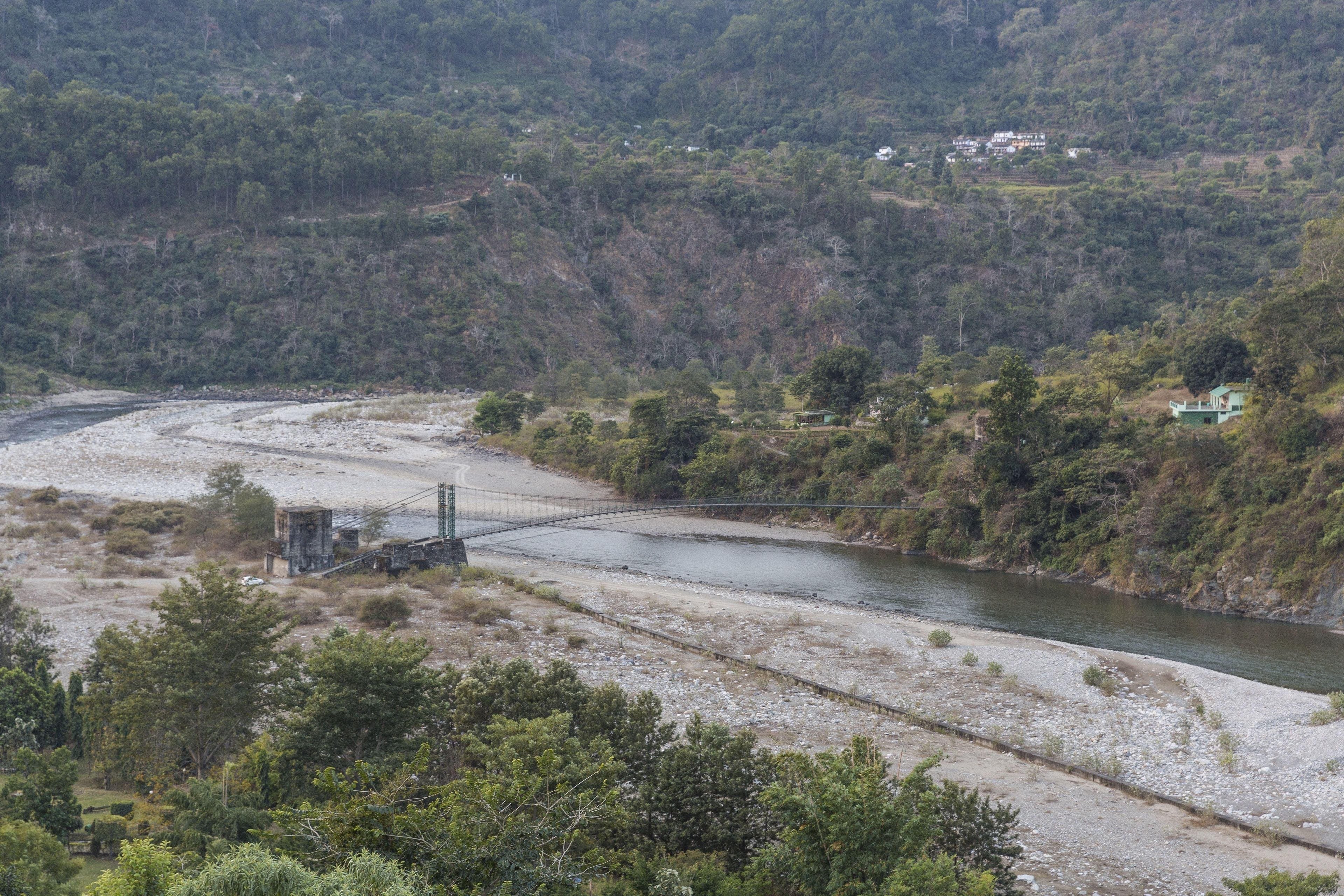 A river with a bridge, surrounded by hills and sparse vegetation.