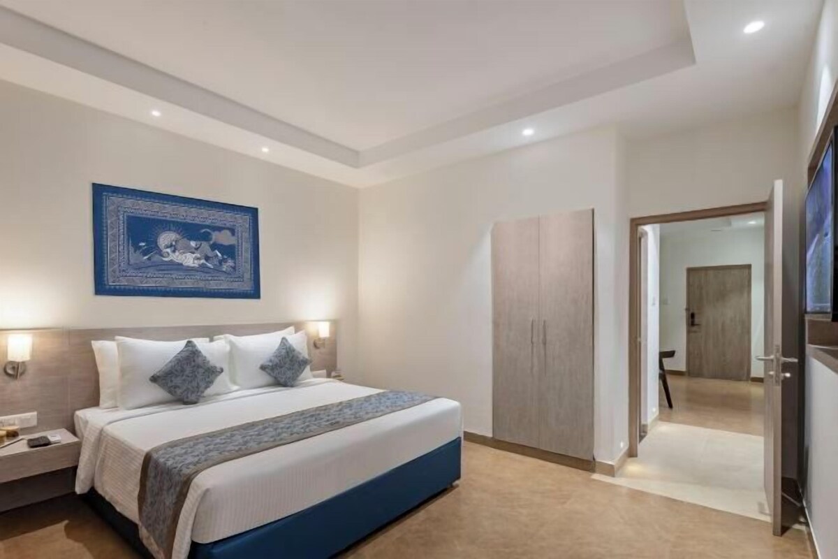 A modern hotel room with a large bed, bedside lamps, a wardrobe, and a framed artwork on the wall.