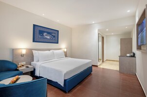 Habitación de hotel con una cama grande, un escritorio con silla, un televisor montado en la pared y una obra de arte enmarcada sobre la cama.