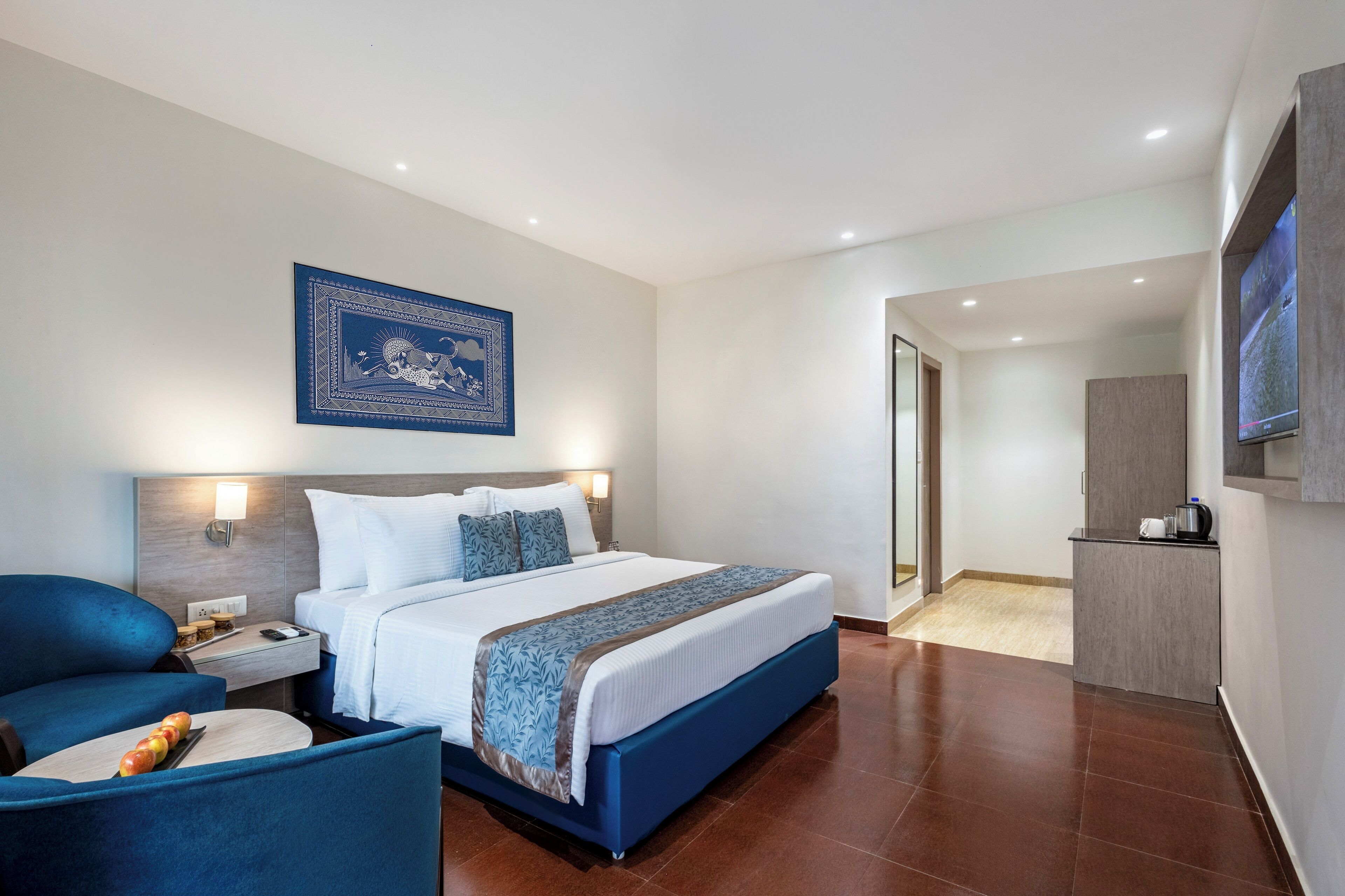 Habitación de hotel con una cama grande, un escritorio con silla, televisor montado en la pared y una puerta que da a un baño.