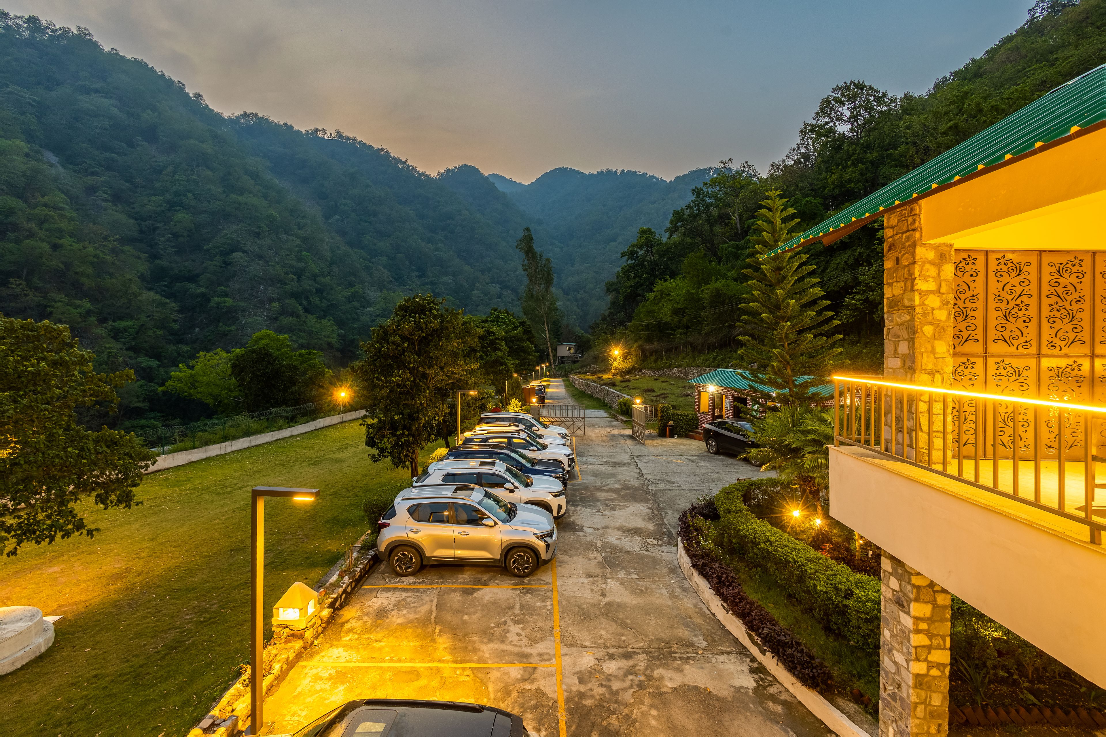A parking area with cars, a building with a green roof, and a mountainous landscape in the background.