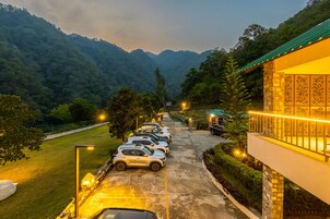 Un estacionamiento con coches, un edificio con techo verde y un paisaje montañoso al fondo.