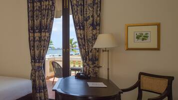 A hotel room with a bed, a table with a chair, a lamp, and a framed picture on the wall.