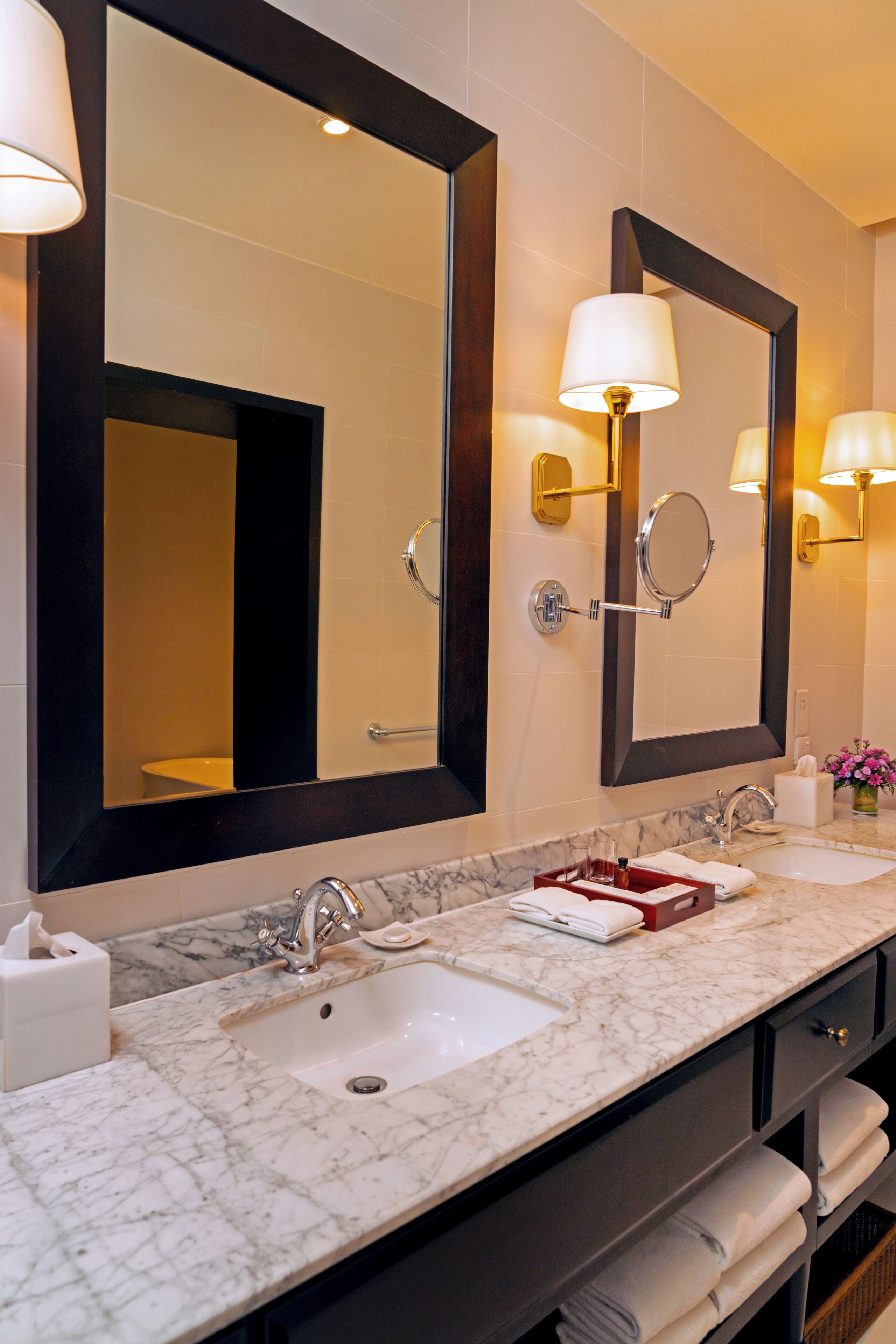 A bathroom with two sinks, a large mirror, wall sconces, and a marble countertop.