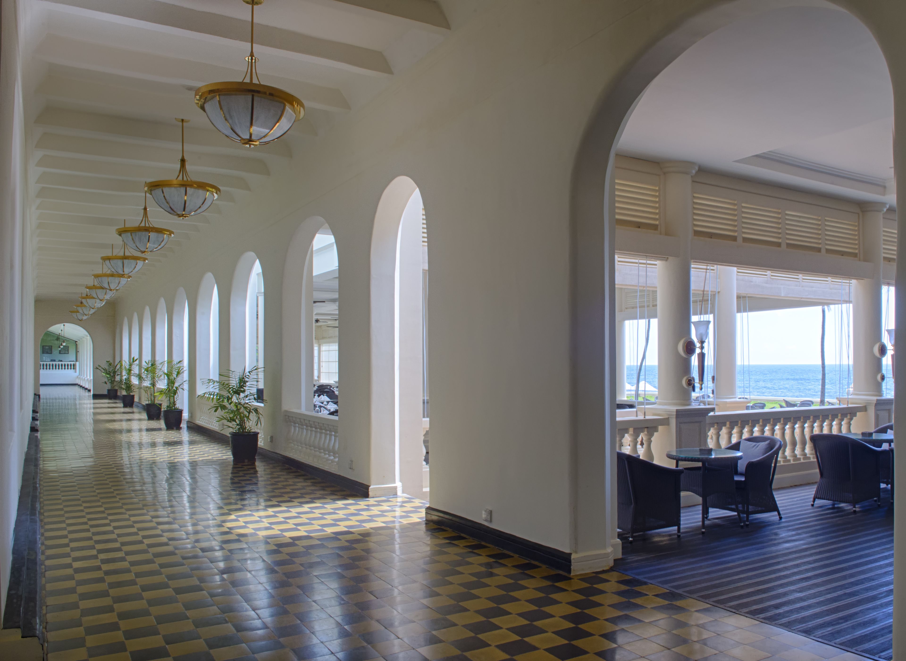 A long corridor with checkered flooring, arched ceilings, and potted plants.