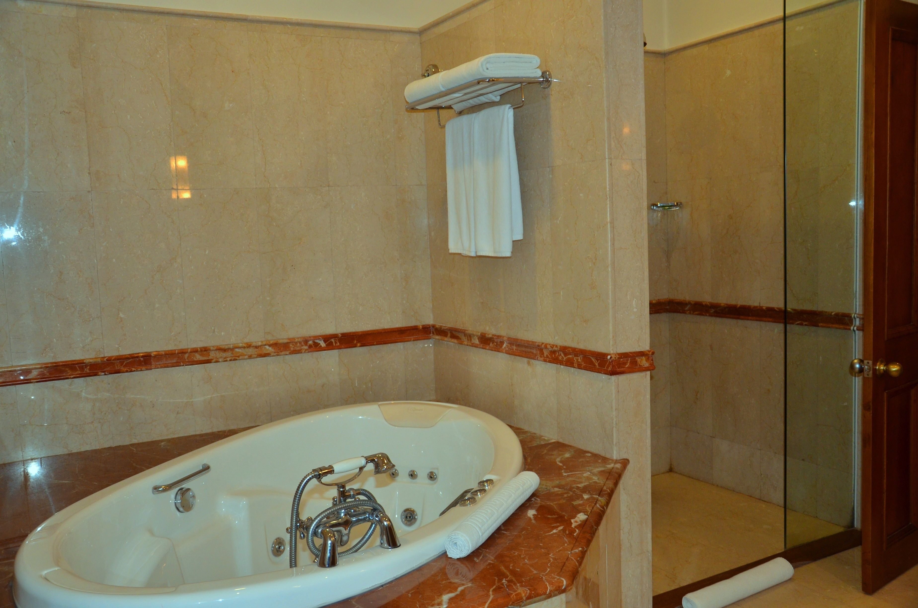 A bathroom with a marble tub, a glass shower enclosure, and a towel rack.