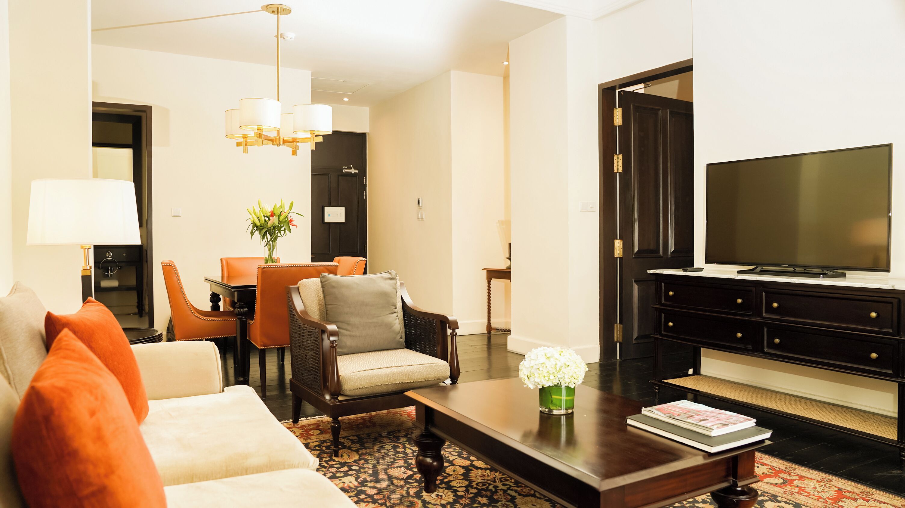 A modern living room with a sofa, armchairs, a coffee table, a TV, and a dining area with a table and chairs.