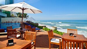 Un restaurante frente al mar con terraza, vistas al océano y una sombrilla grande.