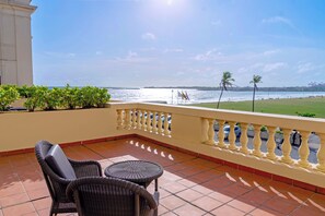 Un balcón con vista al mar, una silla de mimbre y una mesita.
