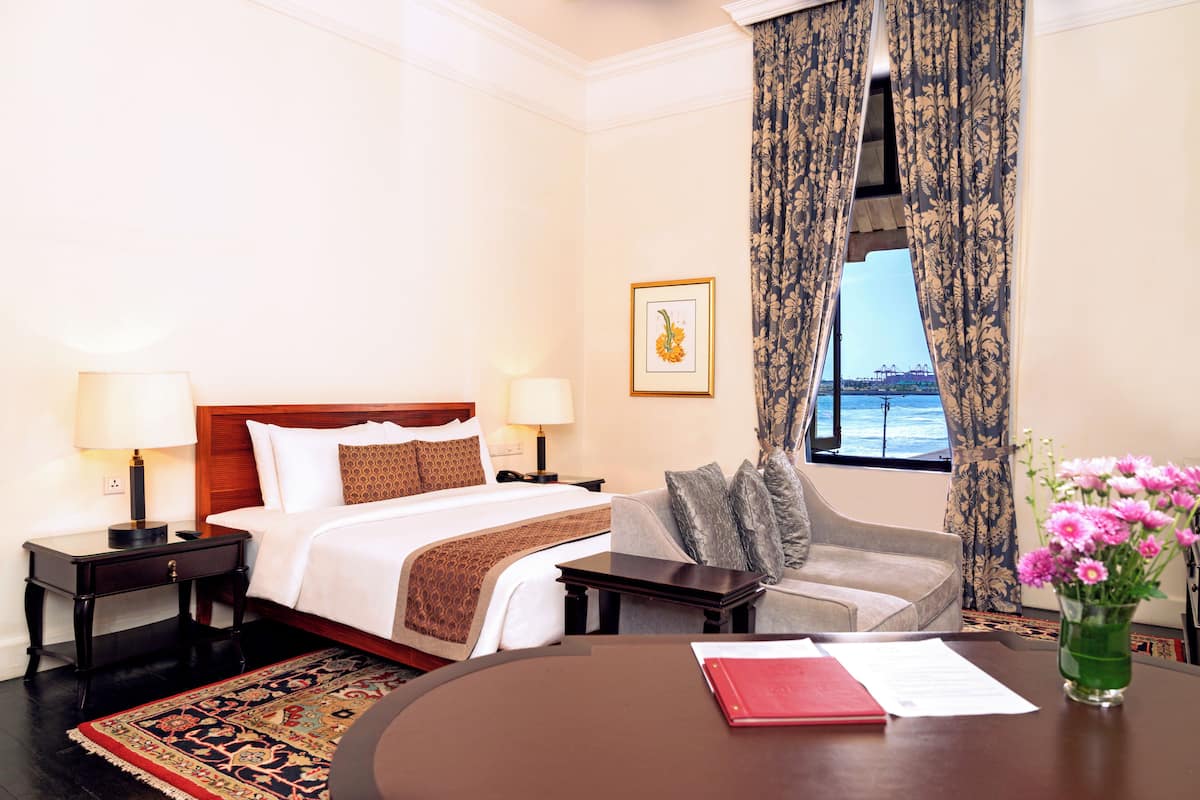 A hotel room with a bed, a sofa, a table with a vase of flowers, and a window with curtains.