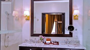 A bathroom with a marble sink, two wall-mounted lamps, a large mirror, and a shower area.