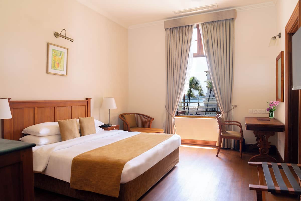 A hotel room with a large bed, two chairs, a small table, and a window with curtains.