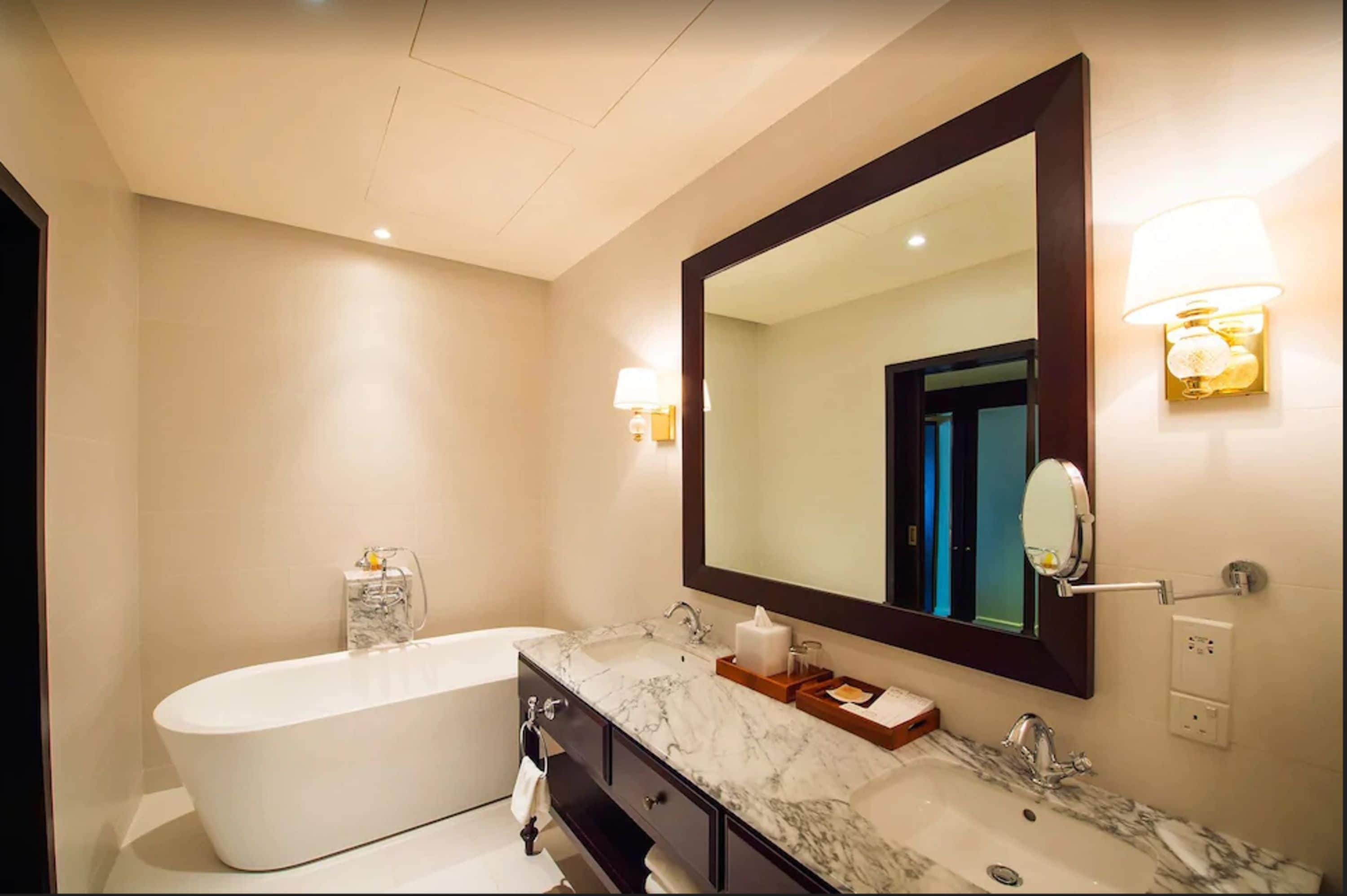 A modern bathroom with a freestanding bathtub, a large mirror, and marble countertops.
