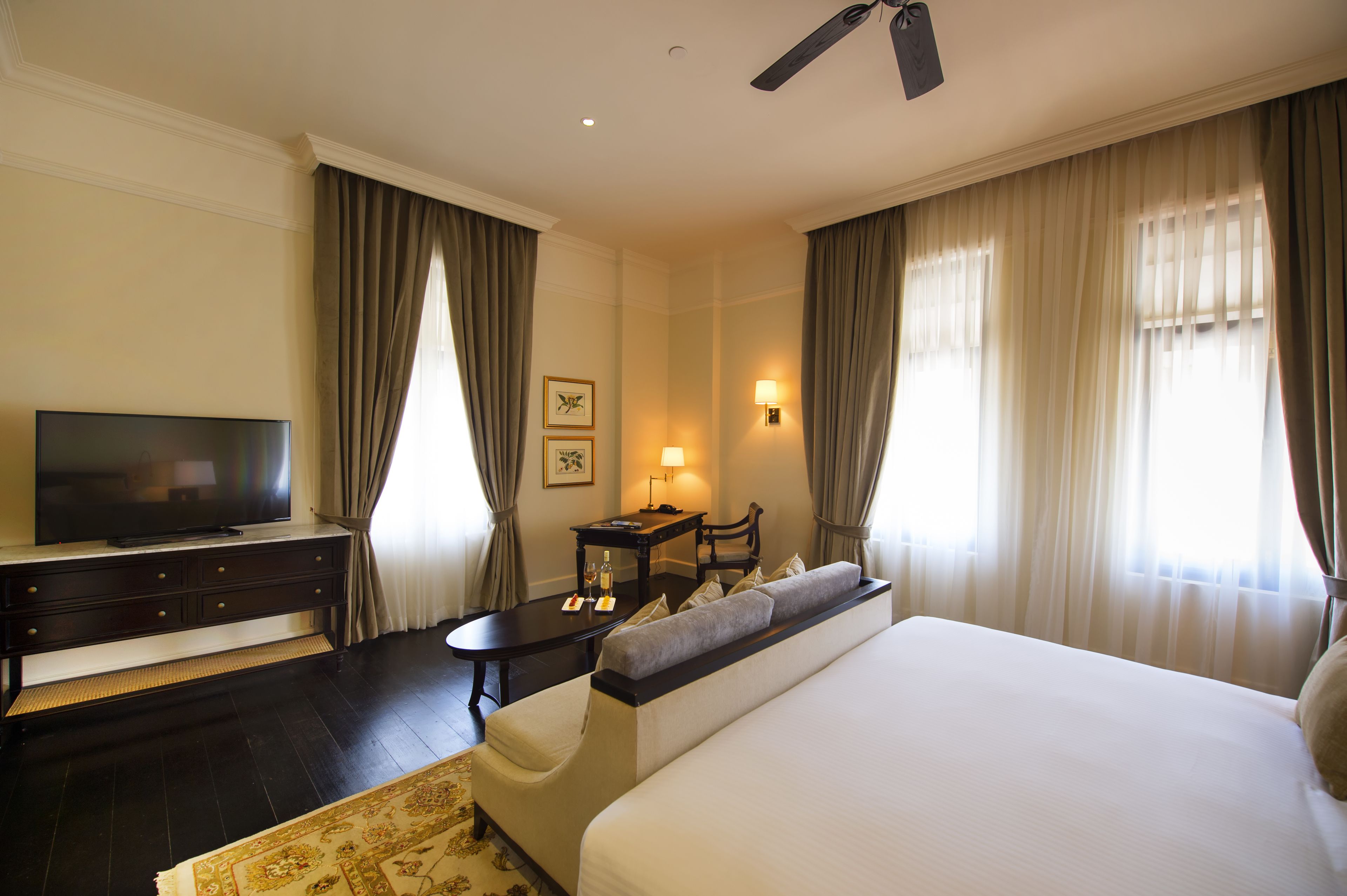 A hotel room with a large bed, a television on a dresser, a desk with a lamp, and curtains on the windows.