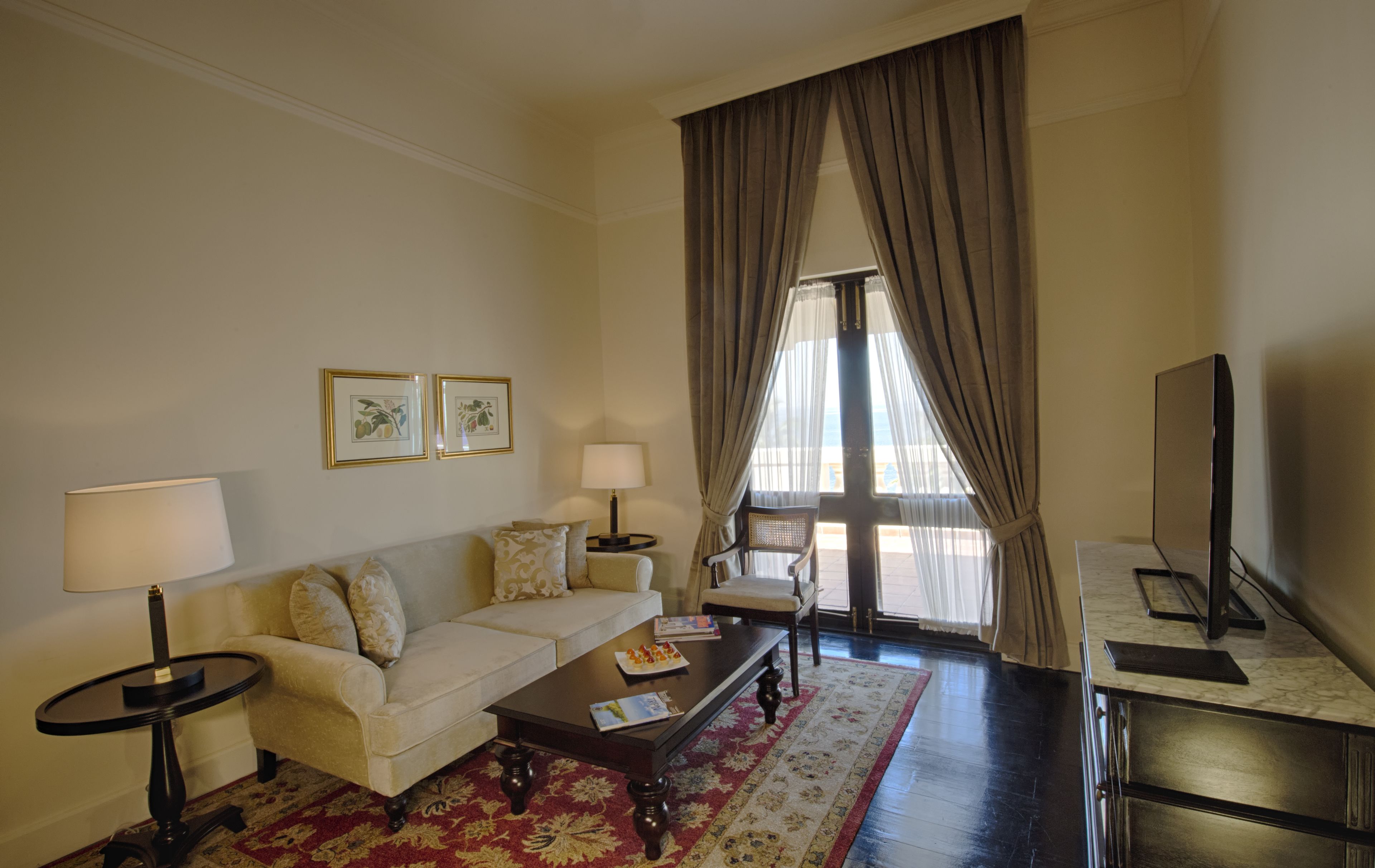 A living room with a sofa, two side tables, a coffee table, a TV, and a large window with curtains.