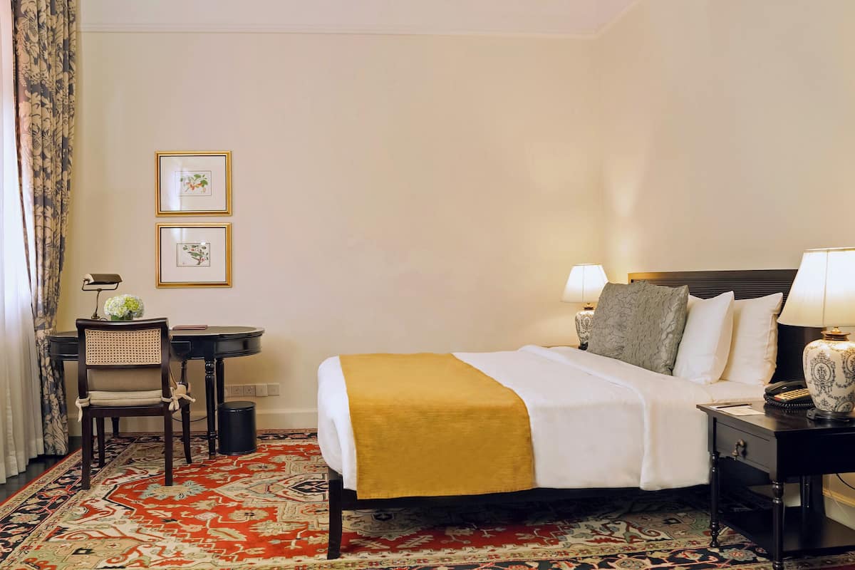 A hotel room with a bed, bedside tables, a lamp, a chair, a small table with a lamp, and two framed pictures on the wall.