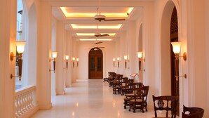 Un pasillo largo y bien iluminado con ventiladores de techo, candelabros y sillas de madera alineadas a un lado.