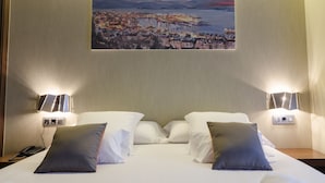 A hotel room with a bed, two bedside lamps, a painting of a coastal town, and a telephone on the nightstand. - Agua de Mar Hotel Boutique (Vigo)