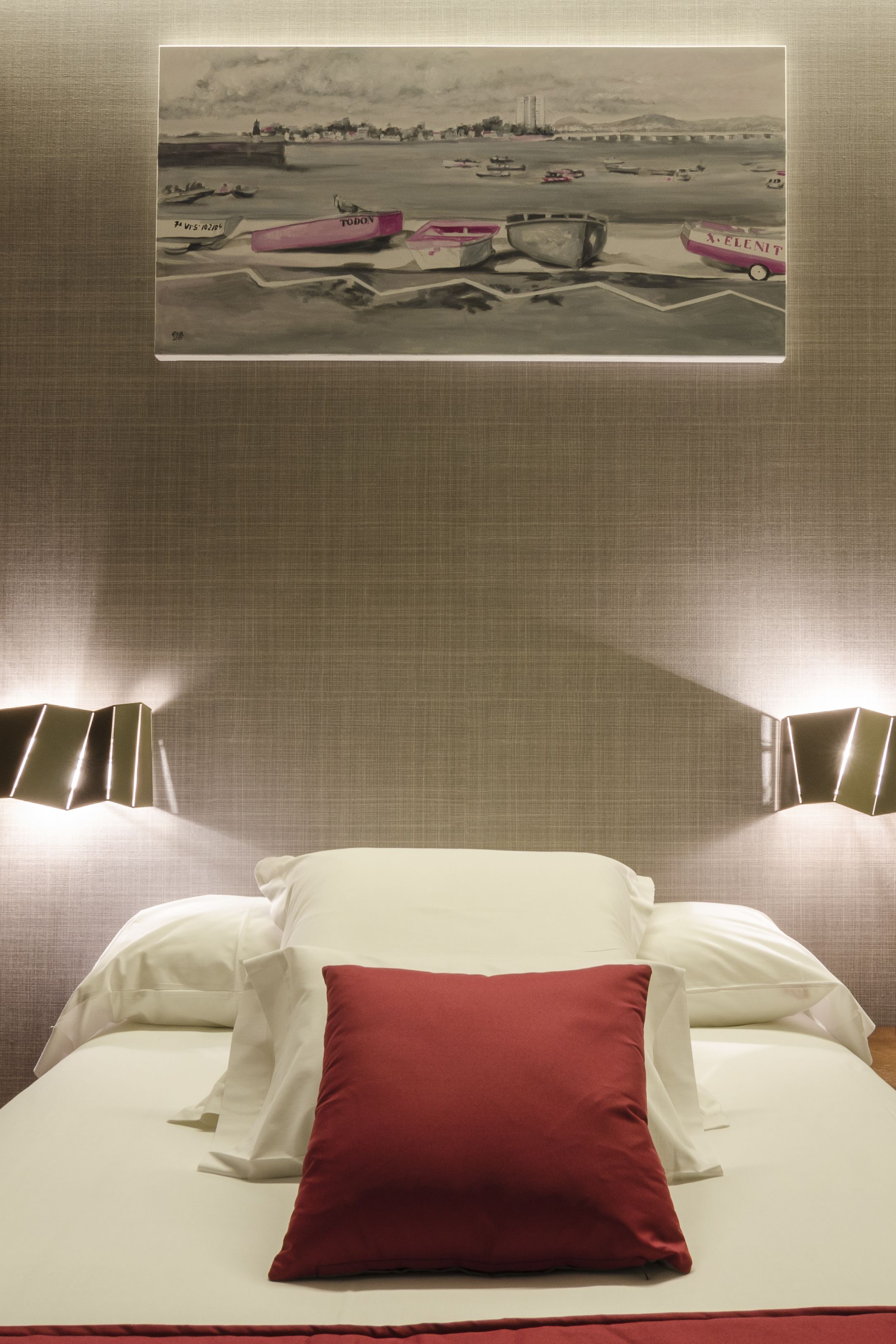 A hotel room with a bed, pillows, and a wall-mounted artwork depicting boats.