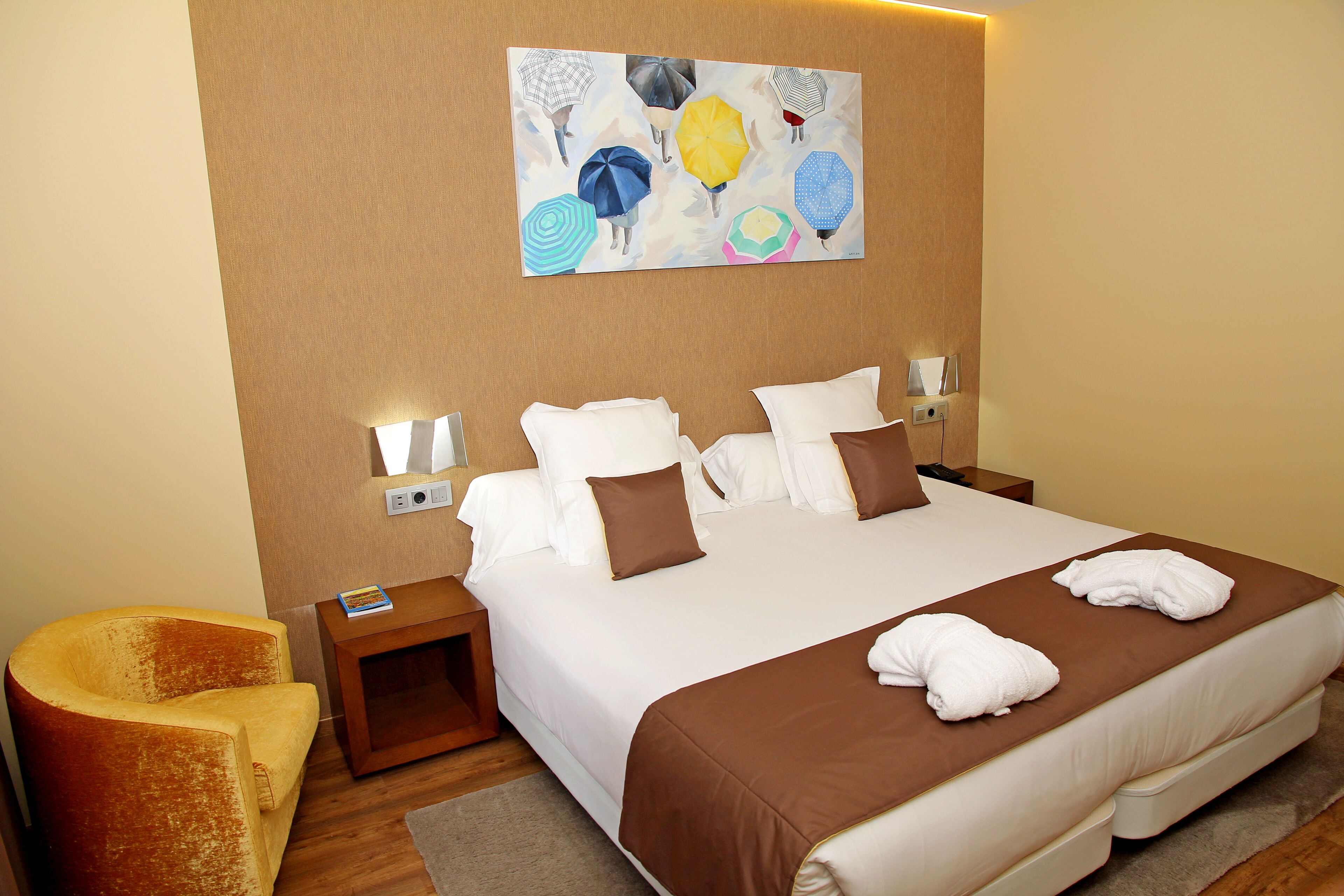 Ein Hotelzimmer mit einem großen Bett, zwei Nachttischen, einem Sessel und einem Bild an der Wand.