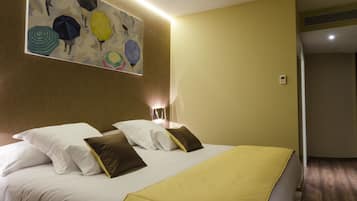 A hotel room with a large bed, white and brown pillows, a yellow bedspread, and a wall art piece of umbrellas.