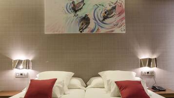 Quarto de hotel com uma cama, dois travesseiros vermelhos, um quadro pendurado na parede e abajures de cabeceira.