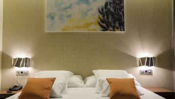 A hotel room with a bed, two bedside lamps, a painting on the wall, and a telephone on the nightstand.