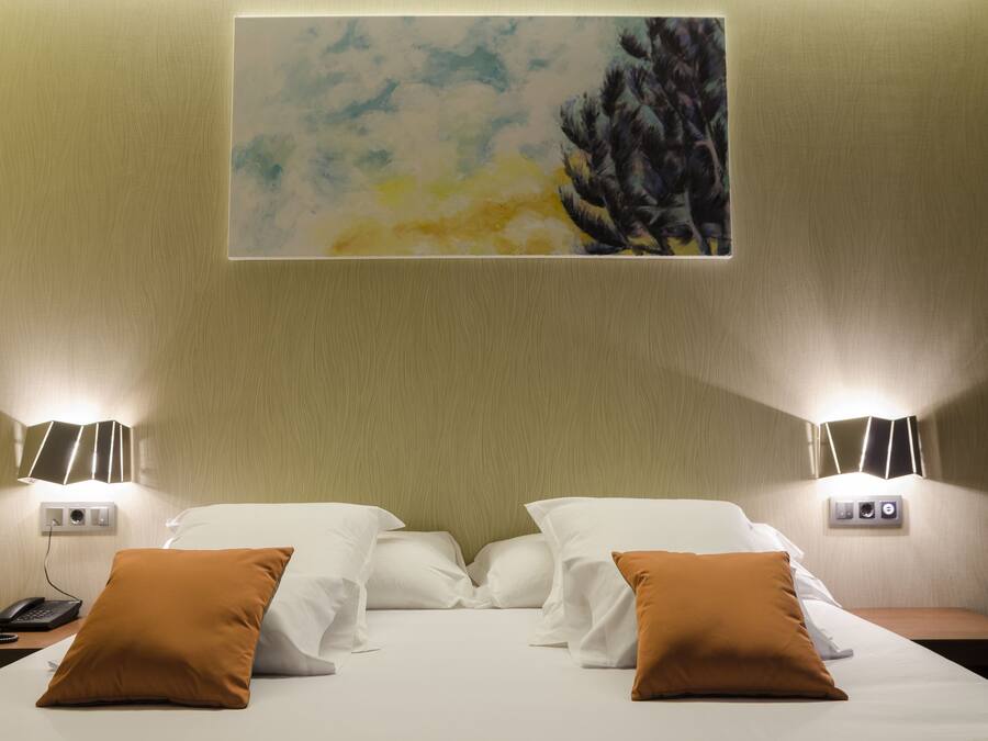 Habitación de hotel con una cama, dos lámparas de noche, un cuadro en la pared y un teléfono en la mesita de noche.